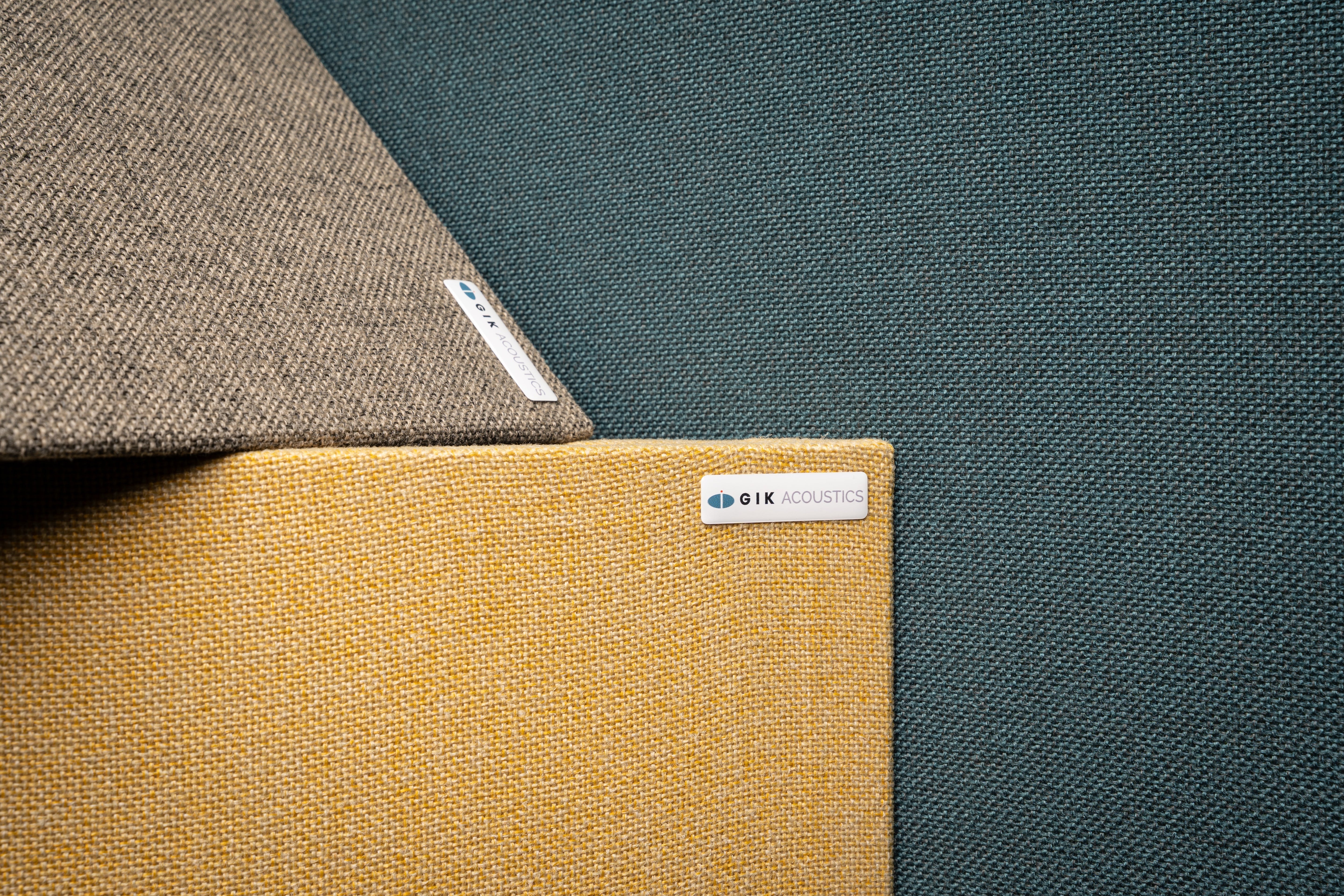 Three GIK Acoustics TriTrap™ Corner Bass Traps stacked together showing fabric colour options in mustard yellow, grey, and teal green.