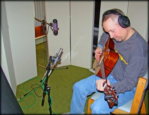 Musician playing guitar in a small recording space using portable acoustic panels for sound control.