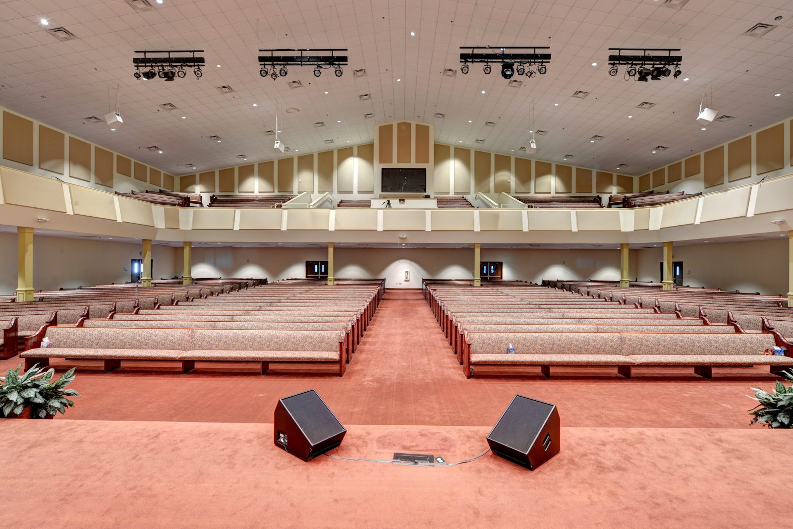 Large church interior with pew seating, balcony, and carpeted stage with speakers, viewed from the front.